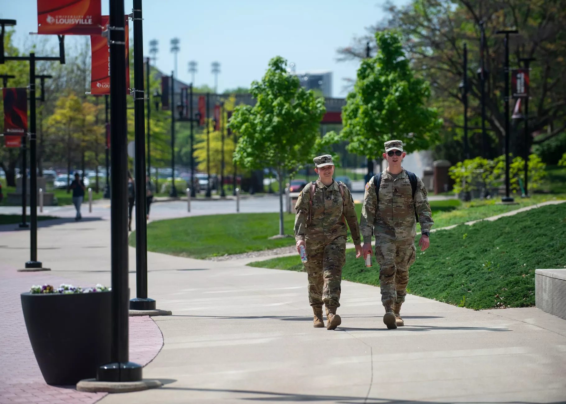 Two students in Army attire walking on campus on a spring day