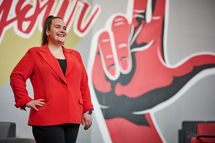 A smiling woman in a red blazer standing in front of an indoor mural.