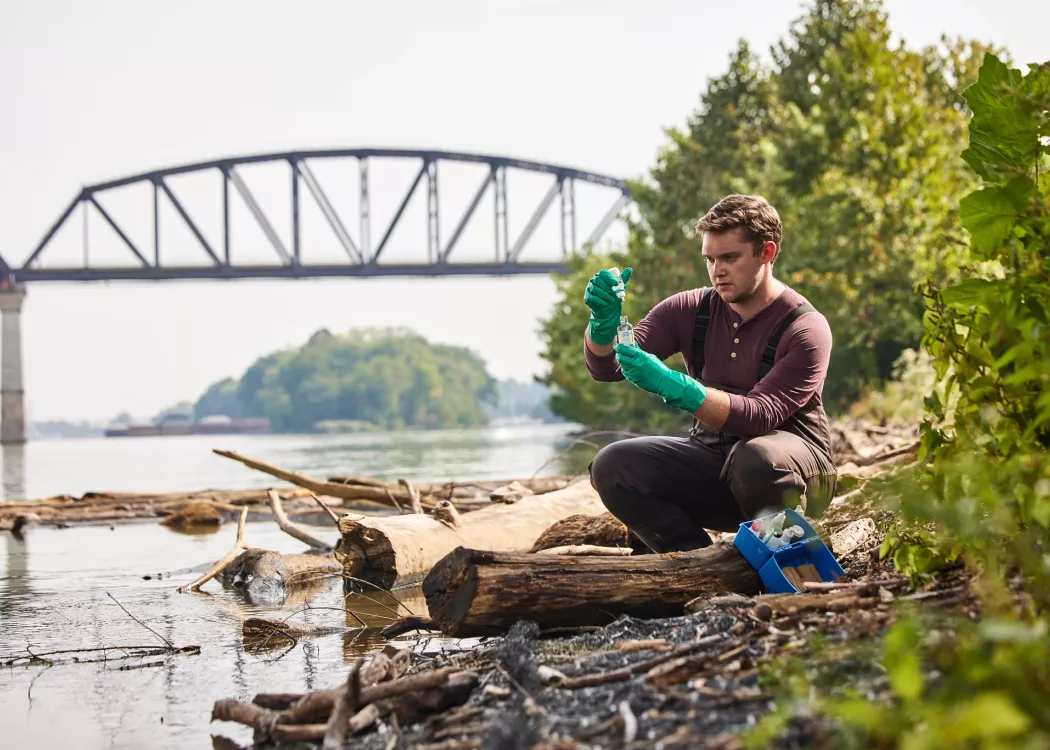 Sam Kessler is testing the water at the Ohio river as he sits close to the edge of the river to retrieve and test the sample.