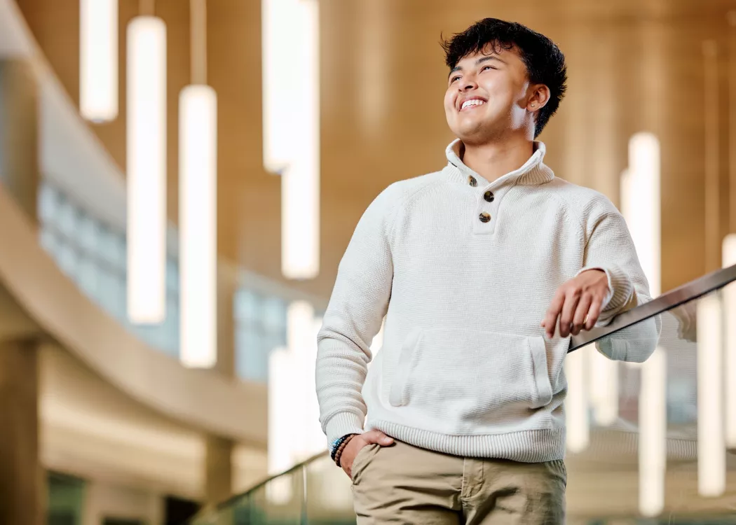 A smiling young male student standing on a modern indoor balcony