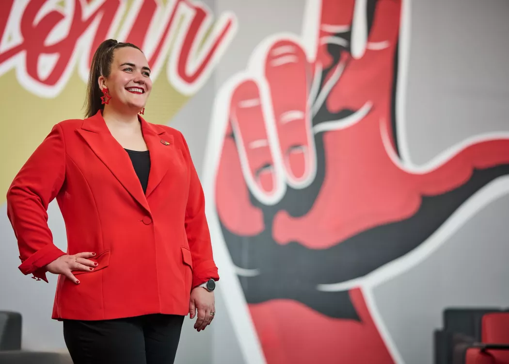 A smiling woman in a red blazer standing in front of an indoor mural.
