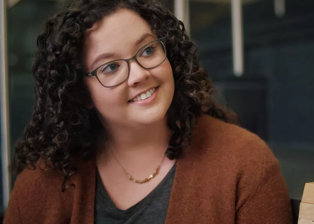A smiling woman with glasses in conversation.