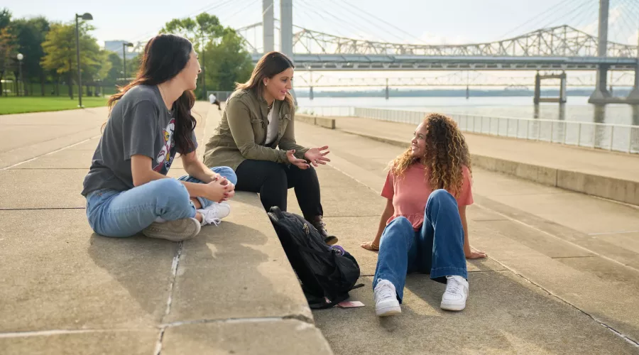 Three students talking on the steps at Waterfront Park in downtown Louisville.