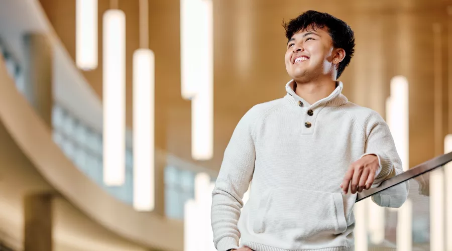 A smiling young male student standing on a modern indoor balcony