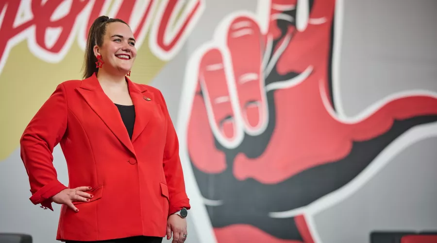 A smiling woman in a red blazer standing in front of an indoor mural.