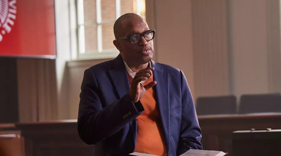 A professor with glasses and holding a book lectures in a school courtroom.