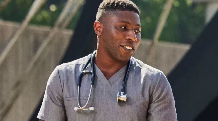 A man in gray medical scrubs with a stethoscope having a conversation outside.