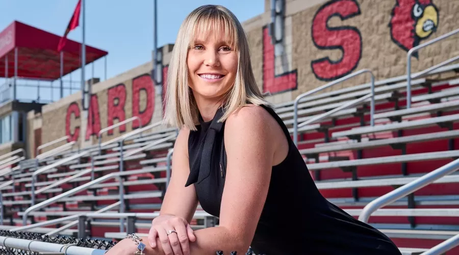 A smiling young woman standing among outdoor stadium bleachers.